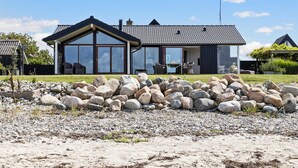 A modern house with a large glass front, a stone wall in front, and a clear sky.