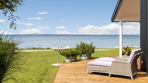 A patio with a wicker sofa and cushions, overlooking a body of water.