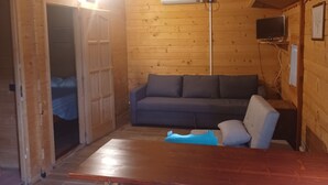 A cozy cabin interior with a wooden floor, a sofa, a table, and a television mounted on the wall. - Bungalow con cucina in agriturismo in campagna immerso nel verde (Lazio)