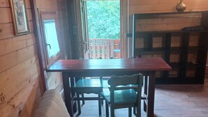 A cozy cabin interior with a wooden dining table, a cushioned sofa, and a view of a balcony. - Bungalow con cucina in agriturismo in campagna immerso nel verde (Lazio)