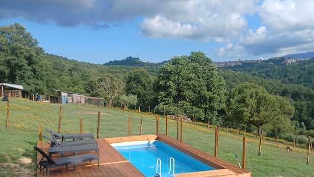A rectangular wooden pool with a ladder, surrounded by a wooden deck, set in a grassy area with a view of a hilly landscape and a clear sky. - Bungalow con cucina in agriturismo in campagna immerso nel verde (Lazio)