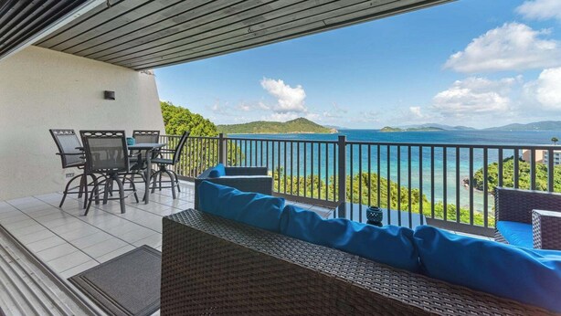 A balcony with a view of the sea, a table with chairs, and a sofa with blue cushions. - The Caribbean Innisfree 1BR/2BA @Point Pleasant/Private Balcony/3 Pools/Beach! (Estate Smith Bay, East End Quarter)