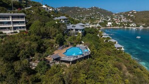 An aerial view of a coastal property with a large swimming pool surrounded by lush greenery, overlooking a clear blue sea with boats. - The Caribbean Innisfree 1BR/2BA @Point Pleasant/Private Balcony/3 Pools/Beach! (Estate Smith Bay, East End Quarter)