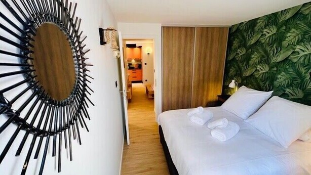 A hotel room with a bed, a wall-mounted decorative mirror, a wooden floor, and a green leaf-patterned wall. - High-end flat in the centre of Gérardmer (Gérardmer)