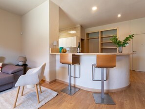 A modern kitchen with white cabinets, a built-in oven, and a bar area with two stools.