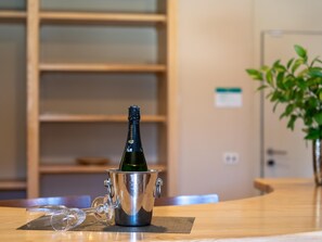 A bottle of champagne in a metal bucket on a wooden table with a glass and a placemat.
