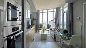 Eine moderne Küche mit integrierten Geräten, ein Essbereich mit Glastisch und Blick auf die Stadt durch große Fenster.