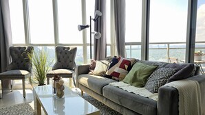Ein modernes Wohnzimmer mit einem grauen Sofa, zwei Sesseln, einem weißen Couchtisch und einem großen Fenster mit Blick auf die Stadt.