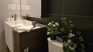 Ein modernes Badezimmer mit einem weißen Waschbecken, dunklen Fliesen und einem Topf mit Pflanze.