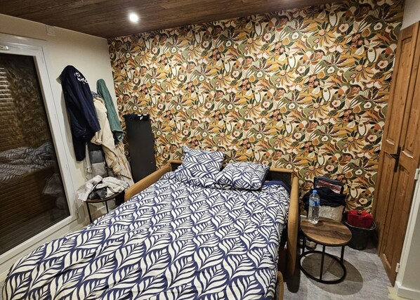 Una camera da letto con parete decorata, un letto con copripiumino a motivi floreali, una testiera in legno e un tavolino con una sedia.