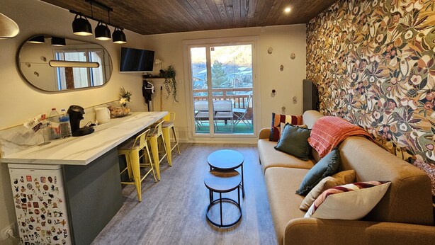 A cozy living area with a sofa, a coffee table, and a dining table with chairs. There's a large mirror and a television on the wall. - Studio with balcony - near lake (Les Deux Alpes)