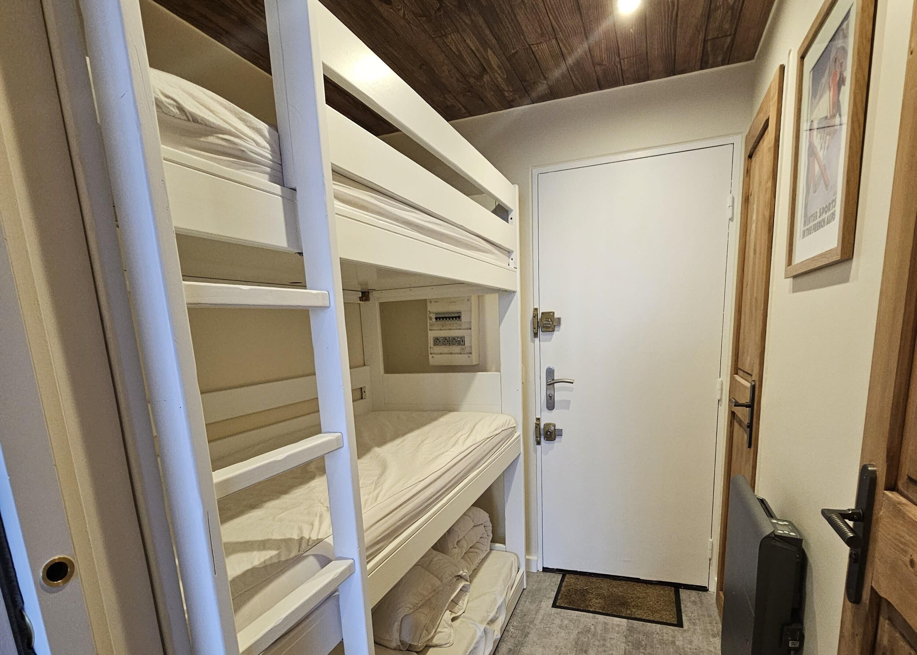 Une chambre avec des lits superposés, une porte et un petit paillasson à l’entrée.