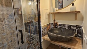 A bathroom with a glass shower enclosure, a stone basin sink, a mirror with a gold frame, and a wall with graffiti-style tiles. - Studio with balcony - near lake (Les Deux Alpes)