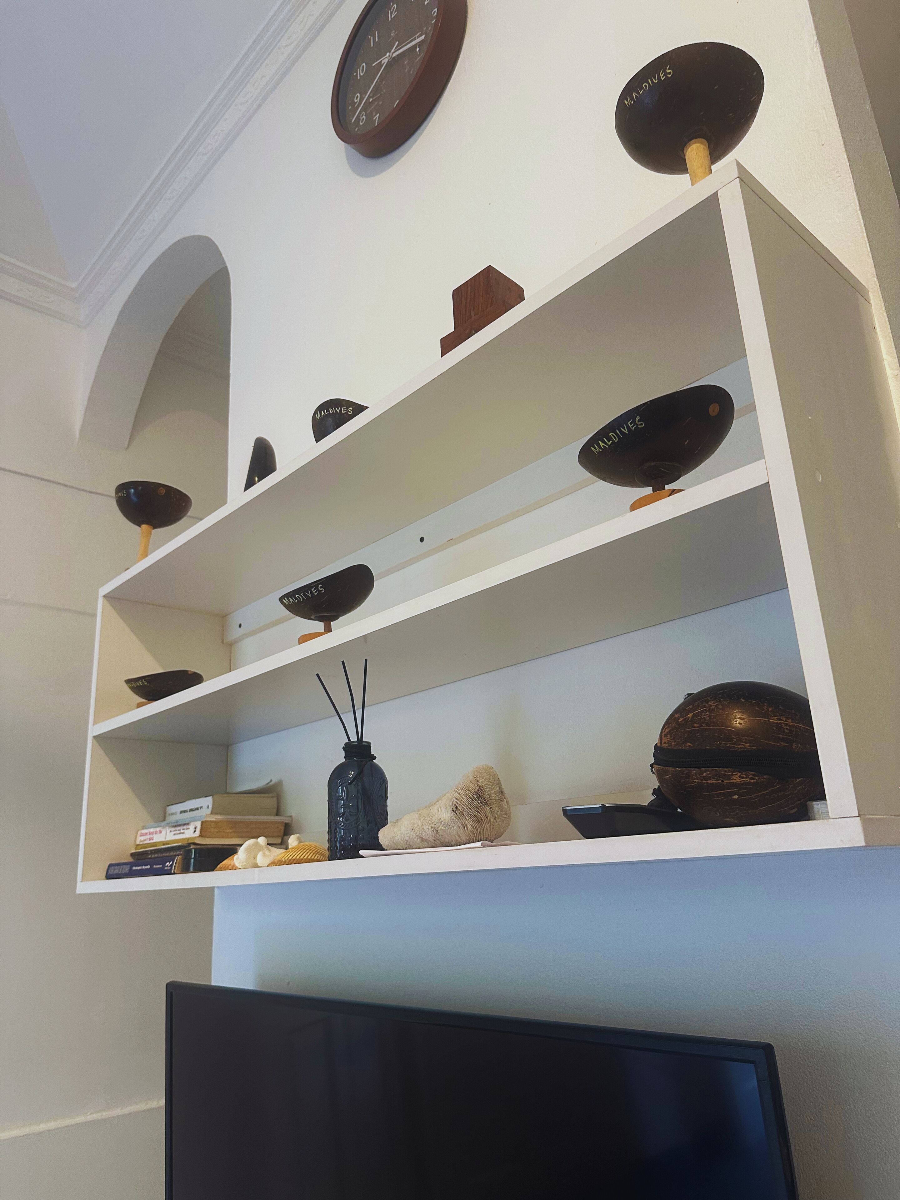 A room with a white wall, a ceiling clock, and shelves with various decorative items.