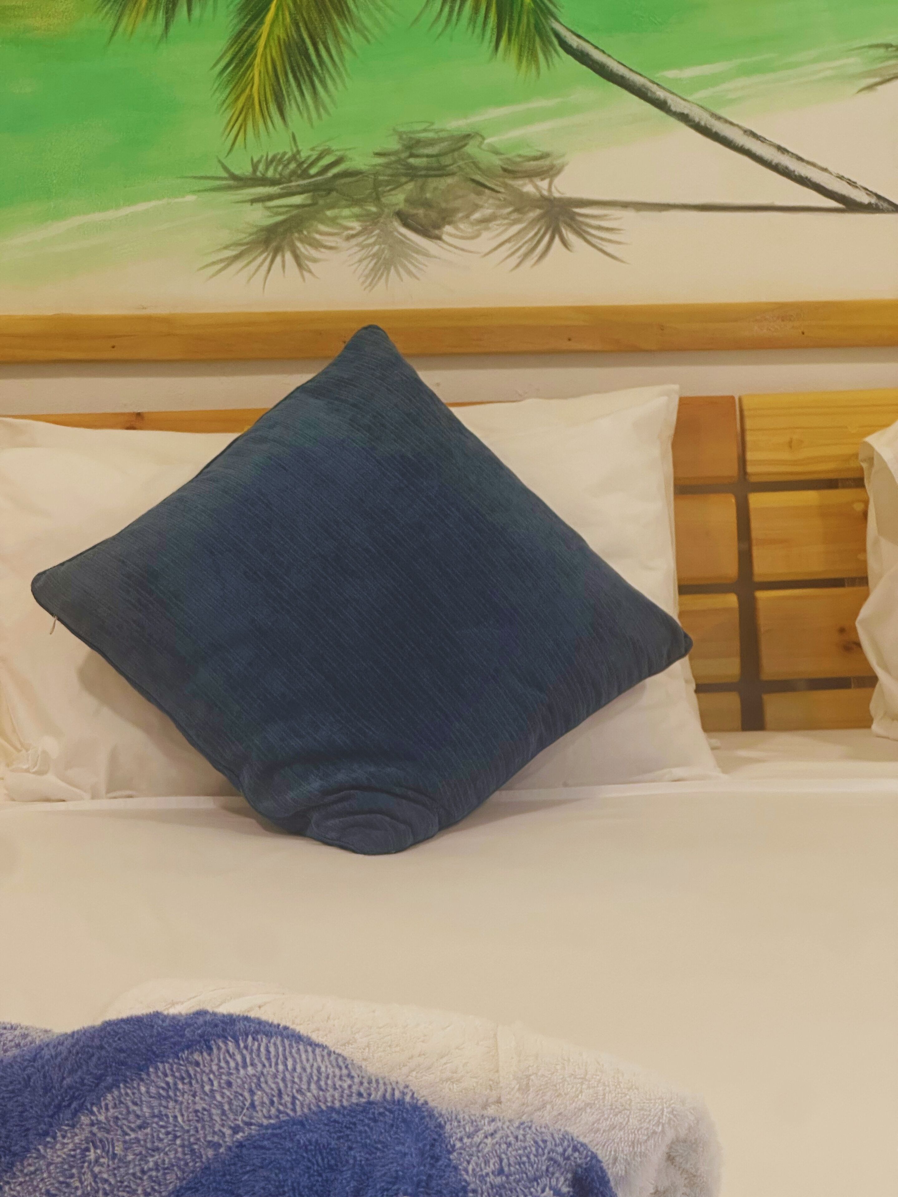 Een bed met een houten hoofdbord, witte kussens en een donkerblauwe kussen.