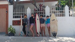 Quatre personnes se tiennent devant un bâtiment dont l'entrée est fermée par un portail, et elles tiennent des planches de surf.