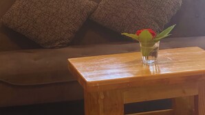 Un banc en bois sur lequel est posé un vase en verre contenant une fleur rouge, placé devant un canapé marron orné de coussins à motifs.