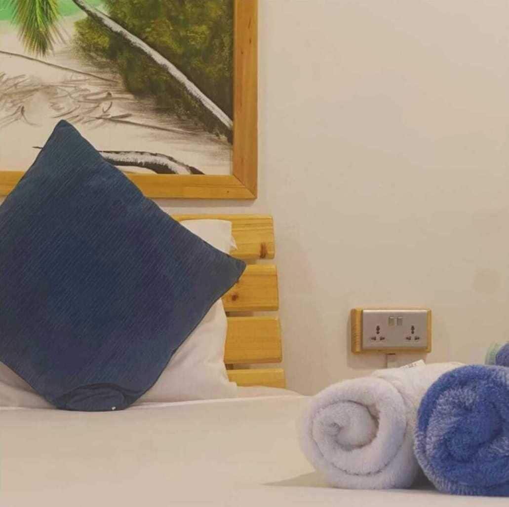 A hotel room with a bed, a wooden headboard, a wall-mounted power outlet, and a painting of a beach scene.