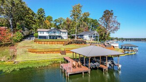 A lakeside property with a dock, a covered seating area, and a large house with a balcony.