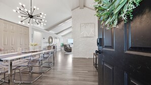 A modern kitchen with a long dining table, chairs, a black refrigerator, and a decorative plant.
