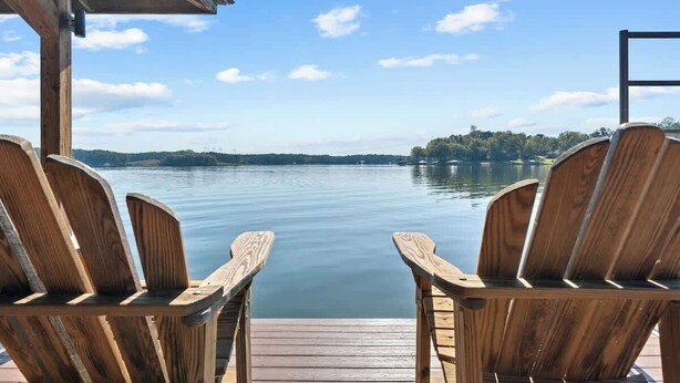 A wooden dock with two Adirondack chairs facing a calm lake.