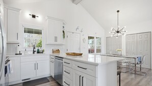 A modern kitchen with white cabinetry, a large island, and a dining area with a glass table and chairs.