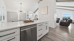 A modern kitchen with white cabinetry, a dishwasher, and a dining area with a table and chairs.