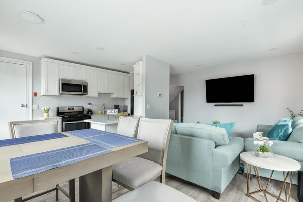 A modern living room with a dining area, a kitchen, and a flat-screen TV mounted on the wall. - Lovely 1-bedroom apartment with Balcony, Wi-Fi, AC - only 30 mins to NYC (New Rochelle)