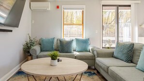 A living room with a grey sectional sofa, a round coffee table, and a TV mounted on the wall. - Lovely 1-bedroom apartment with Balcony, Wi-Fi, AC - only 30 mins to NYC (New Rochelle)