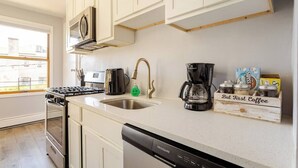 A kitchen with white cabinets, a stove, a dishwasher, a coffee maker, and a coffee bean box. - Lovely 1-bedroom apartment with Balcony, Wi-Fi, AC - only 30 mins to NYC (New Rochelle)