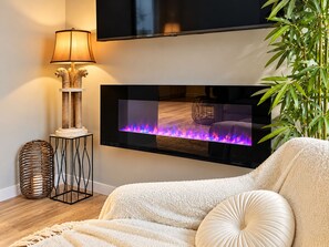 A modern living room with a flat-screen TV mounted on the wall, a decorative floor lamp, a comfortable sofa, and a small side table.