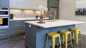 A modern kitchen with grey cabinets, a white island, stainless steel appliances, and yellow stools. - New! The Mel~ Modern, Airy Cottage~5 Mins to Beach + UNCW (Wilmington)