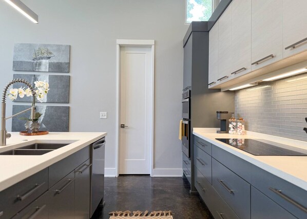 A modern kitchen with grey cabinetry, a central island, and a backsplash of grey tiles.