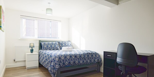 Ein Schlafzimmer mit Bett, Schreibtisch, Stuhl, Nachttisch und einem Fenster mit Jalousien.
