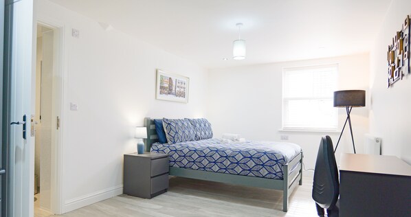 Een slaapkamer met een bed, nachtkastje, lamp en een foto aan de muur.