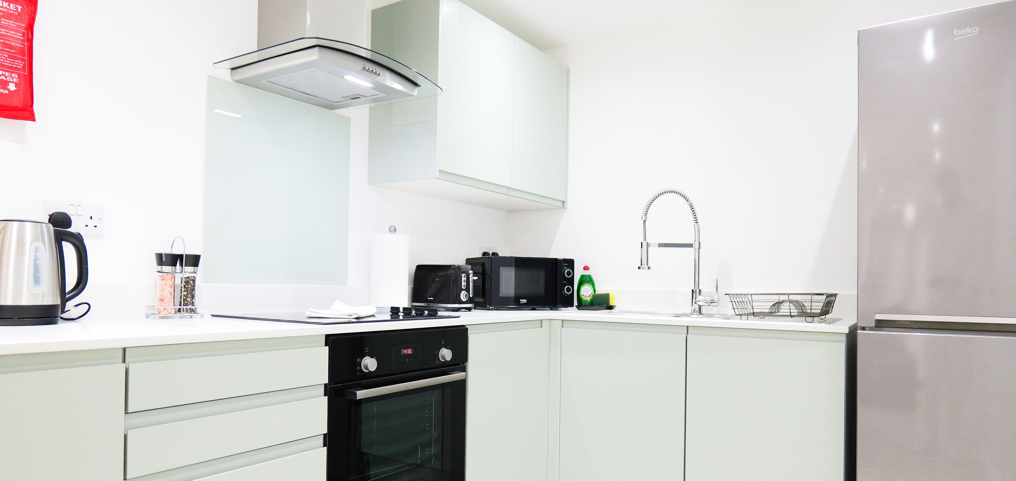 Cocina moderna con refrigerador de acero inoxidable, microondas, hervidor y pileta con grifo.