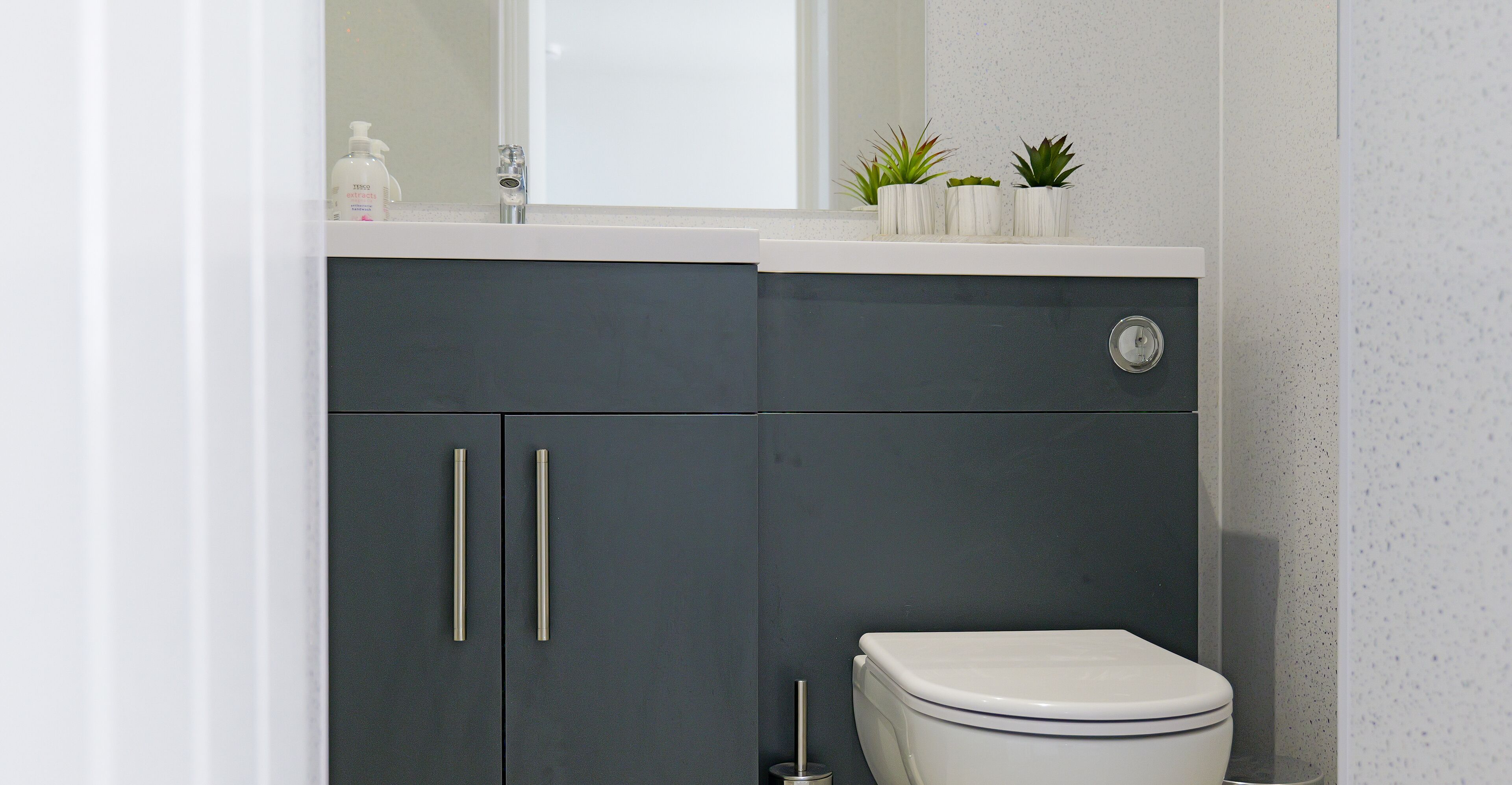 A modern bathroom with a dark cabinet, a white toilet, and three small potted plants on the countertop.