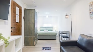 Una habitación de hotel compacta con cama, armario, una pequeña mesa, un sofá y un radiador.
