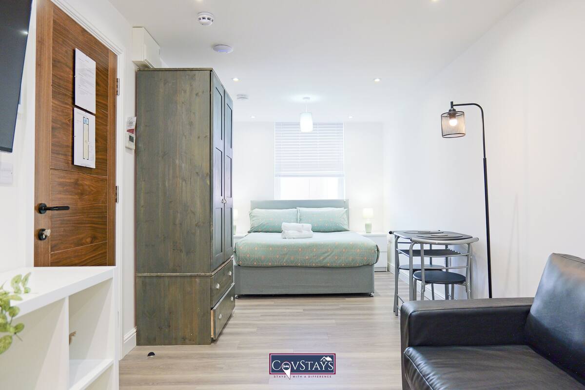 Ein kleines Hotelzimmer mit Bett, Schrank, einem kleinen Tisch, einer Sitzecke und einem Heizkörper.