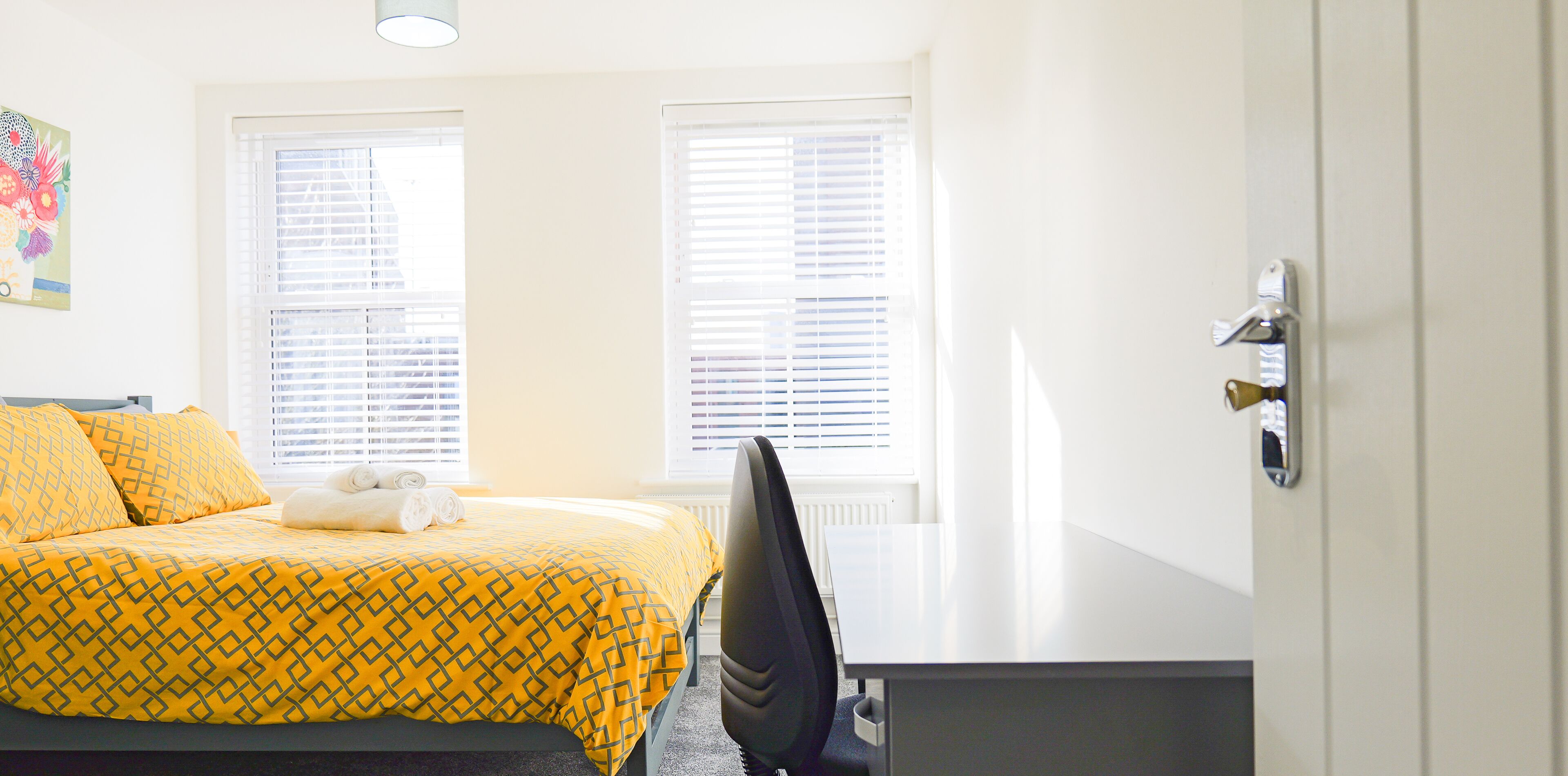 A hotel room with a bed, two windows, a desk, and a chair.