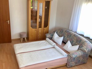 Une pièce comprenant un lit, un canapé à motifs, une armoire en bois et un petit tabouret.