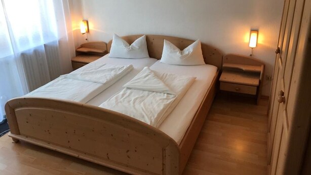 Un dormitorio con cama de madera, dos mesitas de noche y dos lámparas fijadas a la pared.