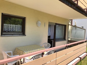 Un balcon avec une table et des chaises, une fenêtre avec un rideau et une porte.