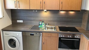 Cocina compacta con gabinetes de madera, lavavajillas de acero inoxidable, horno empotrado y pileta doble.