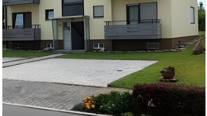 Un edificio residencial de varios pisos con balcones, una entrada central y un camino de acceso de grava.