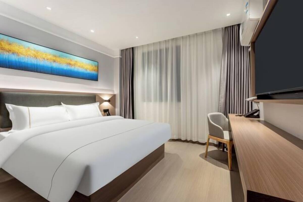A modern hotel room with a large bed, a desk, and a television.