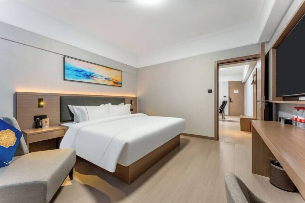 A modern hotel room with a large bed, bedside tables, a TV, and a painting on the wall.