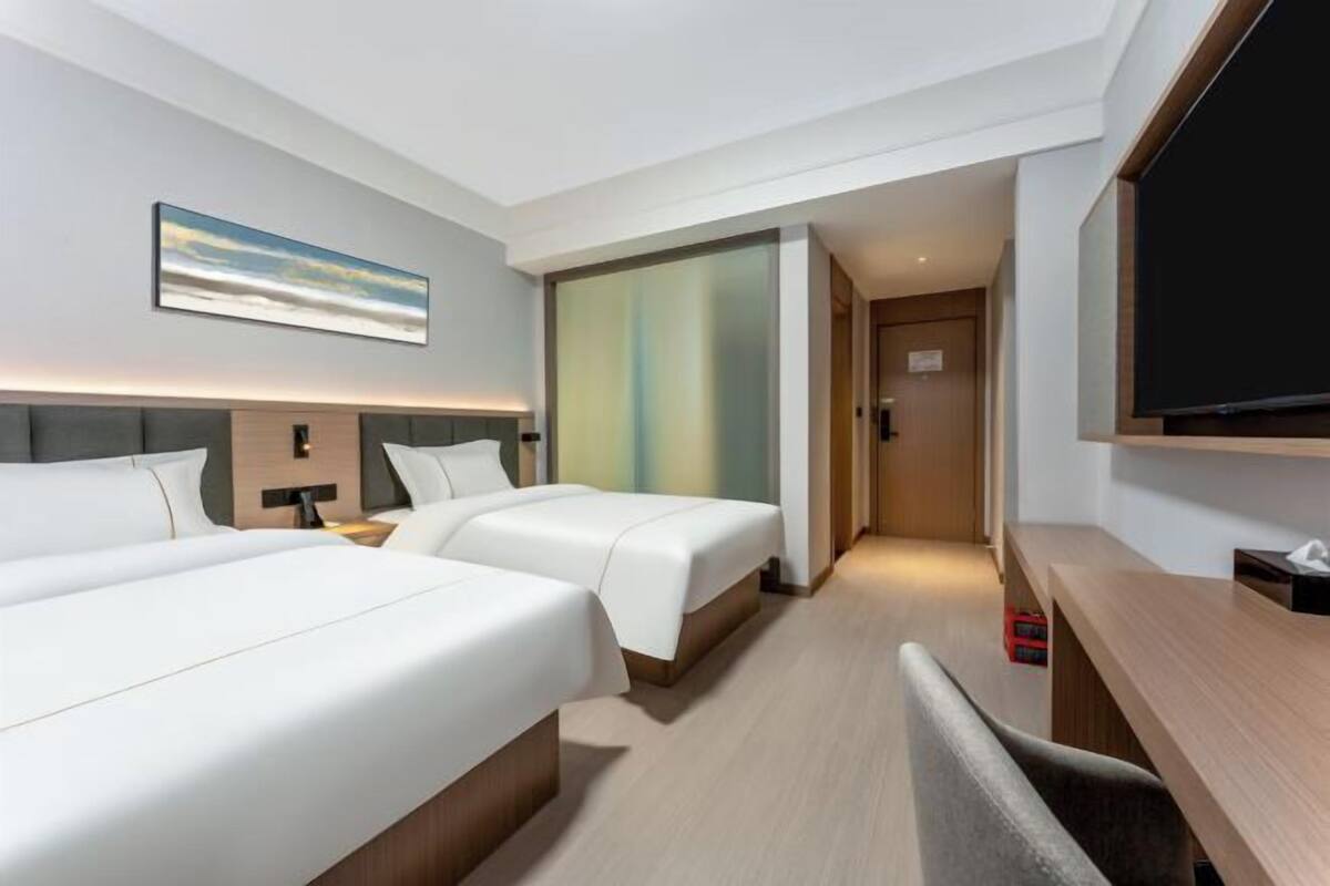 A hotel room with two beds, a desk, a TV, and a painting on the wall.