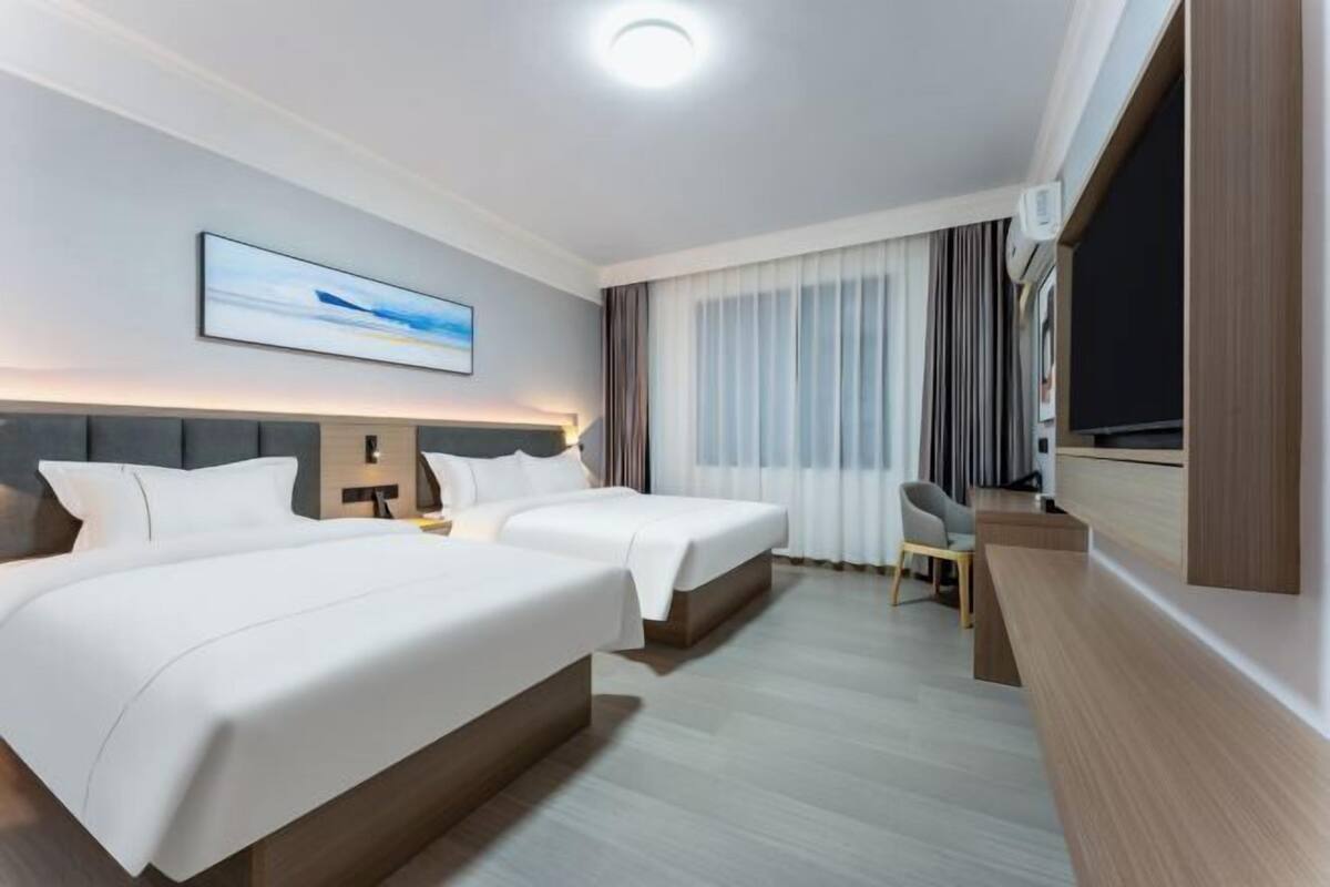 A hotel room with two beds, a desk, a chair, a TV, and a painting on the wall.