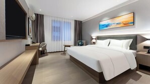 Una habitación de hotel moderna con una cama grande, un escritorio, una silla, un televisor y un cuadro en la pared.
